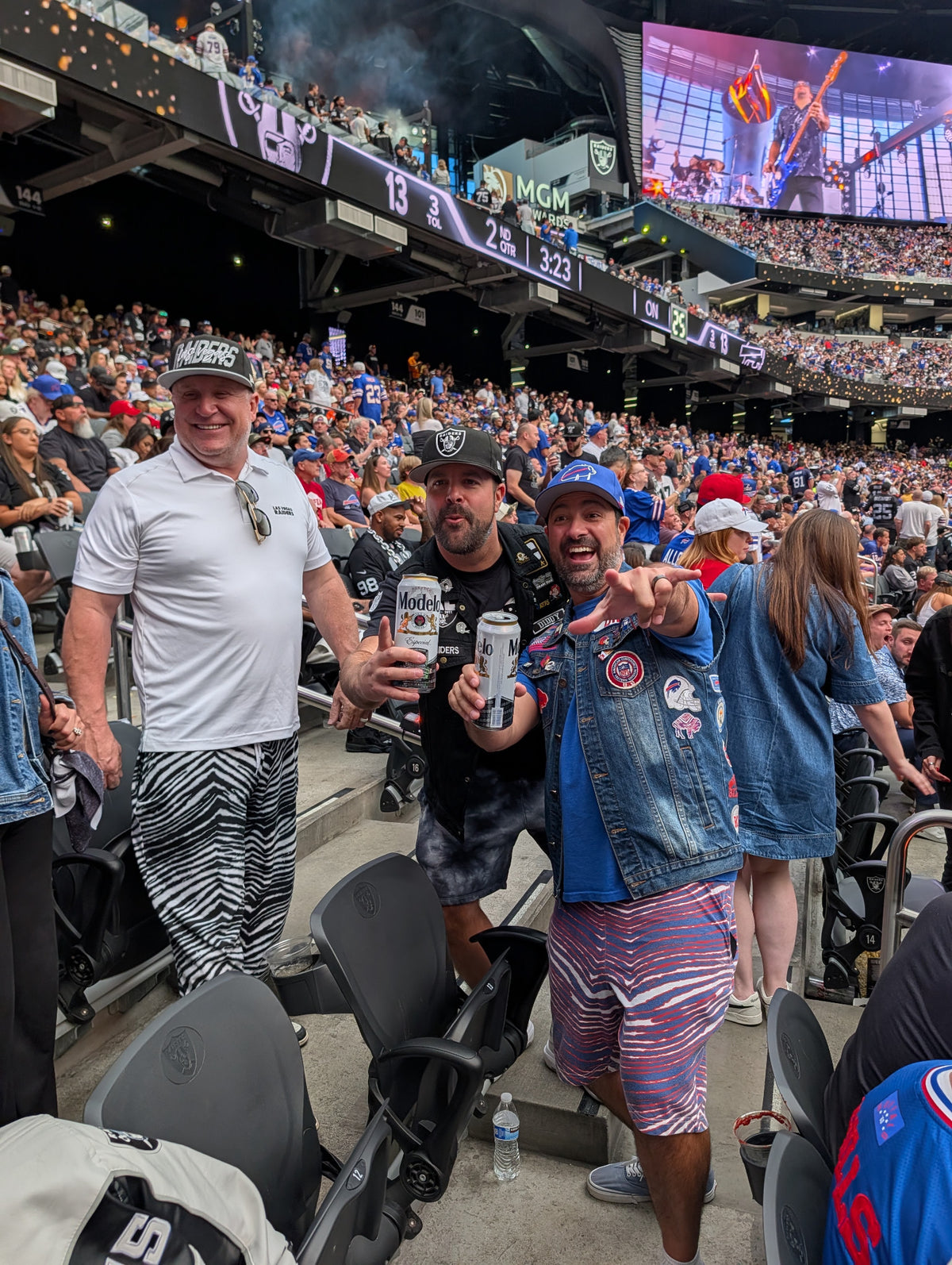 Three football fans wearing black-and-white pants and red-and-blue shorts in a packed stadium